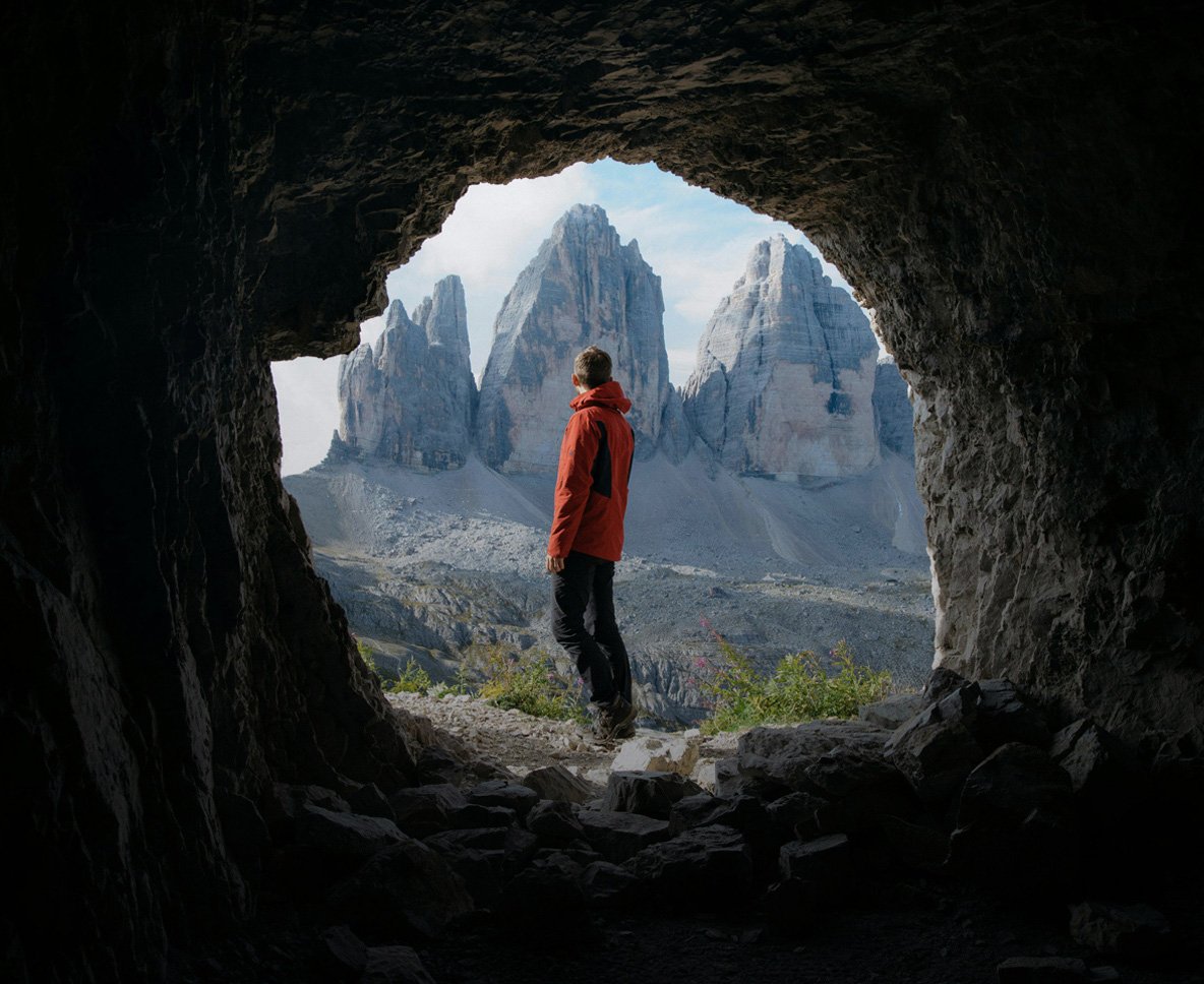 man in cave looking into distant mountains